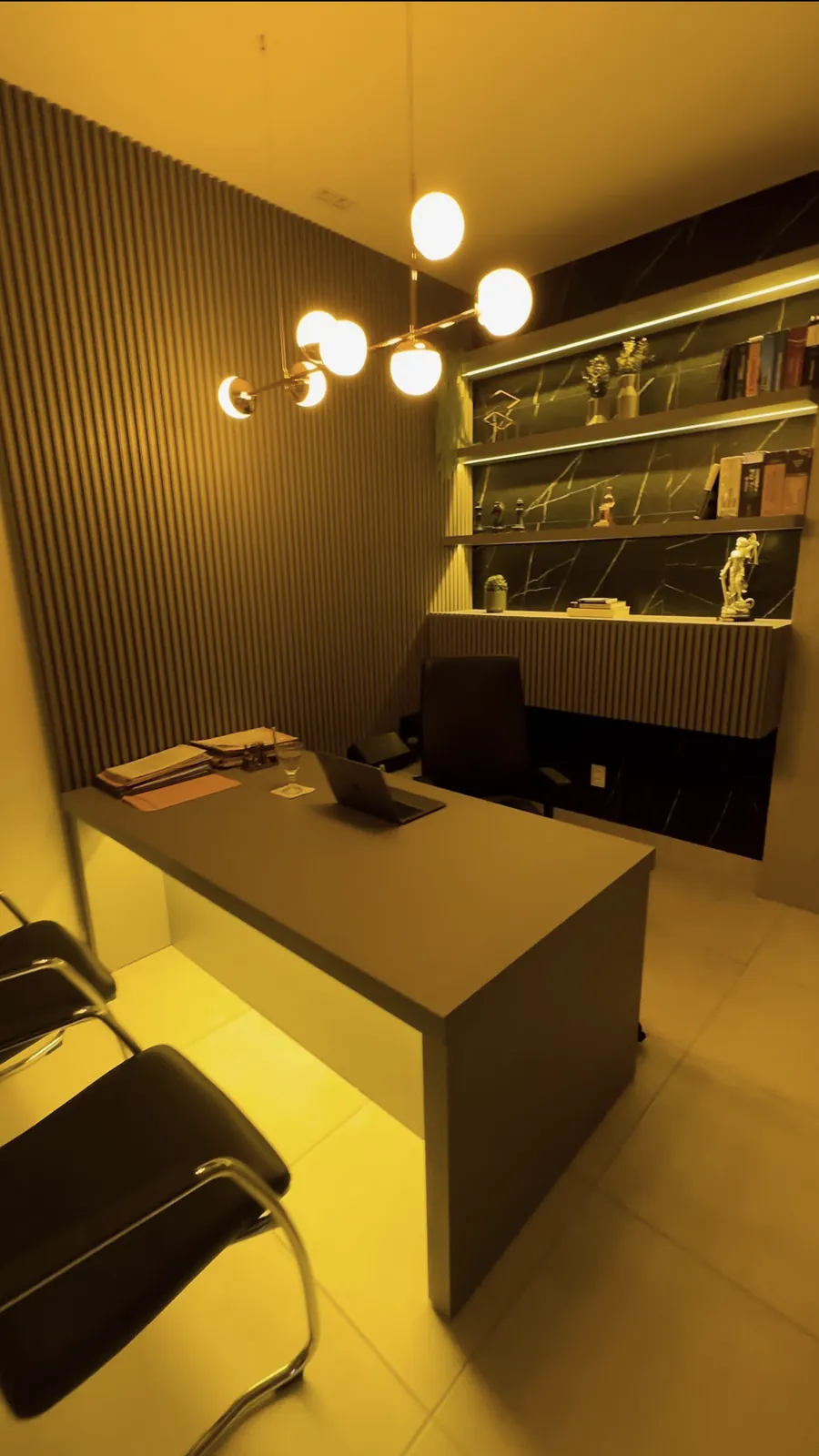Sala de atendimento do escritório, com mesa, estante e iluminação suave